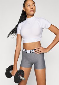 Λευκό κοντό αθλητικό τοπ και γκρι σορτς με ζώνη μέσης "UNDER"; το μοντέλο κρατάει μαύρο αλτήρα; λείο ύφασμα, εφαρμοστή σχεδίαση.