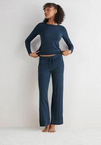 Granatowa bluzka z długim rękawem i pasujące szerokie spodnie wykonane z miękkiego materiału. Koszulka ma delikatny okrągły dekolt i dopasowane rękawy.