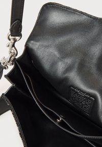 Czarna skórzana torebka o gładkiej fakturze, wyposażona w zamek błyskawiczny, srebrne okucia oraz metkę z logo wewnątrz. Wnętrze posiada wiele przegródek.