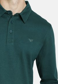 Polo de manga larga verde, hecho de algodón, con cuello abotonado, dos botones y un pequeño logo bordado en el pecho.