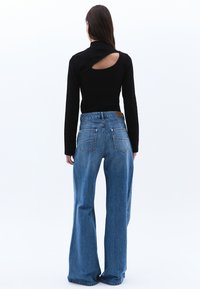 Musta pitkähiha toppi avoimella selkämyksellä, yhdistettynä vaaleansinisii leveälahkeisiin farkkuihin, joissa on takataskut ja ruskea nahkainen merkki.