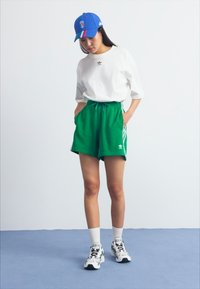 Grønne sportsshorts med hvite sidestreker, en hvit t-skjorte og en blå caps. Joggesko med svarte, hvite og grønne detaljer fullfører antrekket.
