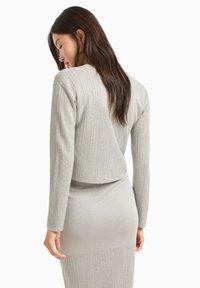 Completo a maglia grigio chiaro composto da due pezzi, con un top cropped a maniche lunghe e una gonna aderente, che mette in mostra un motivo a coste strutturato.