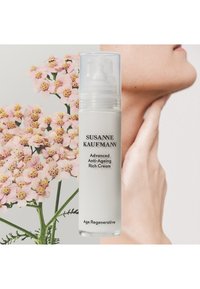 Biała butelka z przezroczystą pompą, oznaczona etykietą "Zaawansowany Krem Przeciwstarzeniowy". Tło przedstawia różowe kwiaty i ludzką skórę.