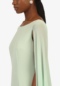 Robe verte menthe avec une silhouette décontractée, des manches courtes et une fente latérale discrète. Tissu lisse et fluide avec un minimum de détails.