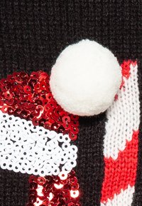 Sweter dzianinowy z czerwonymi i białymi cekinami w wzór Mikołaja, ozdobiony puszystym białym pomponem, na czarnym tle.