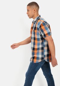 Korte mouwen geruit overhemd in blauw, orangje en marine met een button-down kraag en een enkele borstzak, gecombineerd met donkerblauwe jeans.