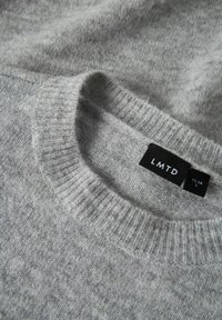 Pull en maille grise présentant un col ras du cou côtelé et une étiquette avec "LMTD" et les détails de taille. Texture douce avec un motif chiné subtil.