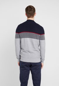 Grå och marinblå tröja med ribbad textur, med ett horisontellt randmönster i ljusgrå och röd accent längs axlarna.