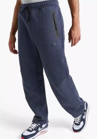 Pantaloni della tuta Nike blu navy con vita con coulisse, tasca laterale con cerniera e polsini aderenti, realizzati in tessuto morbido e strutturato.