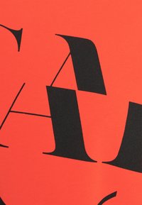 Rode stof met grote zwarte typografie. De letters hebben verschillende vormen en hoeken, wat een gedurfde en grafische patroon creëert.