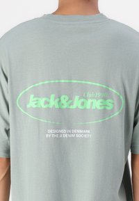 Tricou verde deschis, fabricat dintr-un material moale, cu un guler rotund. Graficul din față include "Jack & Jones" în text alb îndrăzneț și verde deschis.
