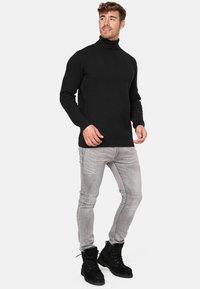 Crna turtleneck pulover sa teksturiranim cik-cak uzorkom, u kombinaciji s svijetlosivim uskim trapericama i crnim čipkastim čizmama.