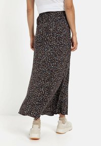 Sort, mønstret maxi-nederdel med en rynket talje. Har et blomsterdesign i blå, brun og beige. Bæres med hvide sneakers.