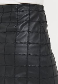 Jupe en cuir noir avec un motif matelassé et des carrés cousus, mi-longue, et d'une texture lisse.