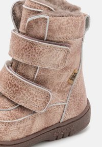 Růžová zimní bota pro dítě s texturou, dvěma suchými zipy, hnědou podrážkou, měkkou huňatou podšívkou a malou látkovou nášivkou TEX na boku.