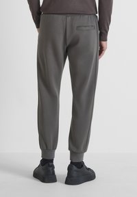 Grijze sportbroek met elastische boorden, voorzien van een achterzak en een gladde textuur. Gekoeld met zwarte sneakers op een neutrale achtergrond.