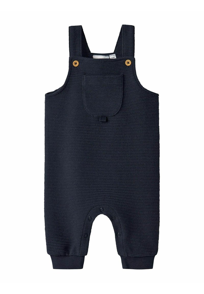Combinaison bébé texturée bleu marine avec bretelles, poche avant avec rabat, boutons en bois et fermetures à pression au niveau de l'entrejambe et des jambes.