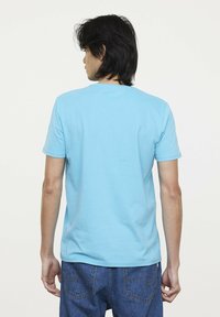 Helles blaues Baumwoll-T-Shirt mit kurzen Ärmeln und rundem Halsausschnitt. Die Rückseite zeigt eine glatte Textur, mit minimalen Details und ohne sichtbare Logos.