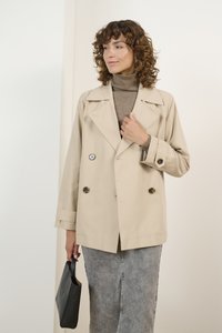 Chaqueta beige de doble botonadura con grandes botones negros y marrones, combinada con un cuello de tortuga marrón claro y una falda de denim gris. Bolso negro.