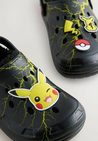 Zwarte klompen met een geel bliksemontwerp, versierd met Pikachu- en Pokébal-decoration. Ontworpen met ventilatiegaten en een gestructureerd oppervlak.
