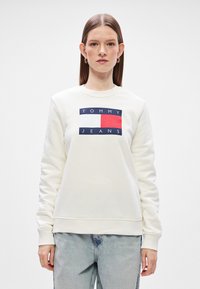 Λευκή μπλούζα με στρογγυλή λαιμόκοψη, με λογότυπο σε ναυτικό μπλε, κόκκινο και λευκό στο κέντρο. Μαλακό υλικό με ριμπ μανσέτες και στρίφωμα.