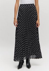 Zwarte plissé maxi-rok met witte stippen, met een zachte textuur en een tailleband, gecombineerd met zwarte haklaarzen.