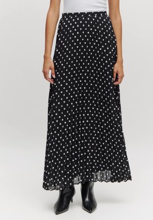 Zwarte plissé maxi-rok met witte stippen, met een zachte textuur en een tailleband, gecombineerd met zwarte haklaarzen.