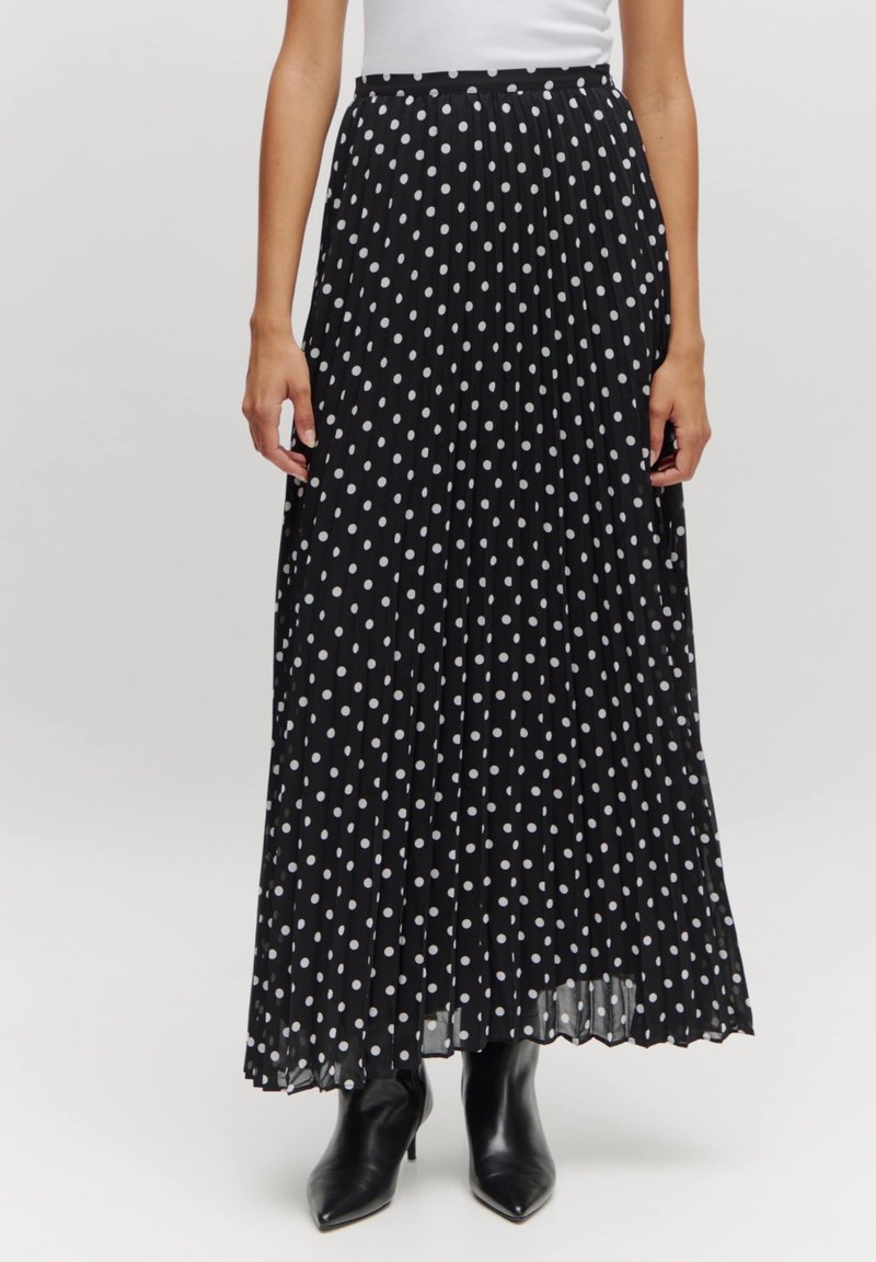 Zwarte plissé maxi-rok met witte stippen, met een zachte textuur en een tailleband, gecombineerd met zwarte haklaarzen.