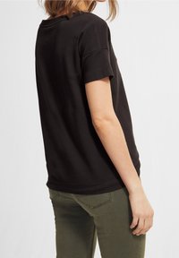 T-shirt nera a maniche corte realizzata in tessuto morbido, con una vestibilità comoda. Indossata con pantaloni verde oliva, che mostrano i dettagli dell'orlo sul retro.