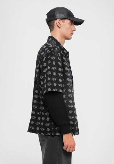 Black short-sleeve shirt with white diamond and floral pattern, paired with a black long-sleeve top and black leather cap.