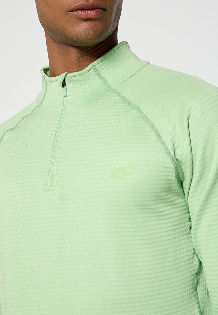 Pull-over zippé vert clair avec une surface texturée, doté d'un col montant, d'une courte fermeture éclaire et d'un petit logo sur la poitrine.