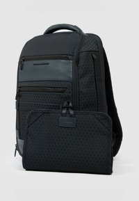 Mochila negra hecha de tela texturizada con un patrón de diamantes. Cuenta con múltiples compartimentos con cremallera y una bolsa frontal desmontable.
