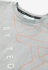 Grå bomulds t-shirt med orange grafiktryk og tekstureret skrift. Ribbet krave og mærke synligt indeni halsudskæringen.