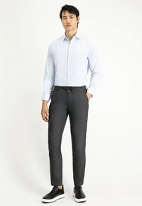 Lichtblauw gestreept shirt met een button-down kraag, gecombineerd met grijze broek met trekkoord en zwarte sneakers met witte zolen.