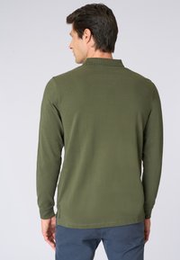 Camicia a maniche lunghe verde oliva con una texture morbida e un orlo dritto. Presenta un colletto a coste e un sottile dettaglio del logo vicino al fondo.