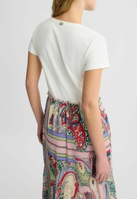 Haut blanc à manches courtes avec une taille froncée et un fermoir décoratif à l'arrière. Comprend une jupe à motifs colorés avec des rayures verticales et des motifs floraux.