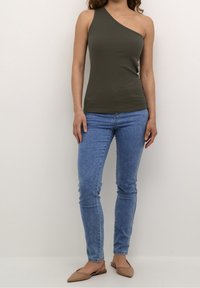 Olijfgroene geribbelde mouwloze top met een asymmetrische halslijn, gecombineerd met lichtblauwe slim-fit jeans en beige puntige platte schoenen.