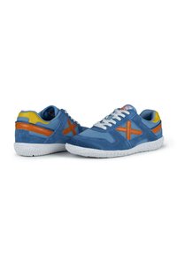 Zapatillas deportivas azules que combinan materiales de malla y gamuza, con suelas texturizadas blancas y acentos en naranja y amarillo en el talón y los laterales.