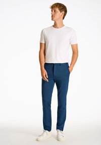 Marineblaue Hose mit taillierter Passform, aus glattem Stoff. Kombiniert mit einem eng anliegenden weißen Hemd und weißen Turnschuhen. Schlichtes Design, ohne Muster.