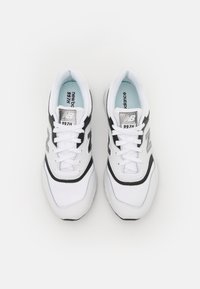 Pár bílých a černých tenisek New Balance 997H se šněrováním, viděných shora na bílém pozadí.