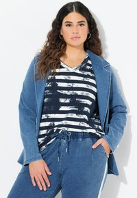 Blazer de denim en azul claro, con cuello con muescas; camisa a rayas en blanco y negro; pantalones de cordón a juego con acentos laterales.