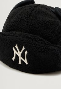Căciulă neagră din fleece cu logo-ul brodat alb al New York Yankees pe față, dotată cu urechi.