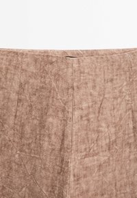 Gros plan d'une jupe en tissu de lin beige montrant la taille avant avec des coutures subtiles et des plis naturels de la texture.