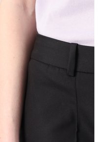 Pantalon noir en tissu lisse, doté d'une ceinture plate et de poches latérales. Coutures visibles le long des coutures et silhouette ajustée.