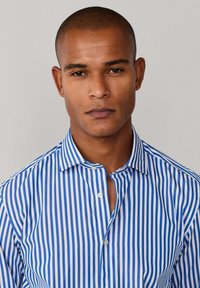 Chemise en coton rayée bleue et blanche avec col boutonné et texture subtile, dotée d'une coupe ajustée et de boutons visibles le long de la patte de boutonnage.