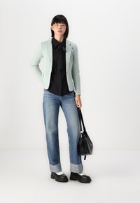 Světle mátově zelený blazer, černý top s mašlí, modré široké džíny, černá kabelka a silné černé boty s bílými ponožkami.