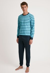 Lichtblau gestreepte blouse met lange mouwen en zwarte afwerking; gecombineerd met donkerblauwe, toelopende broek. Zachte stof met een gladde textuur.