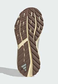 Hnedá gumová podrážka s hlbokými drážkami, béžová medzičlenková časť a trojuholníkový akcent. Obsahuje textúrovaný vzor pre trakciu a stabilitu.