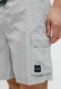 Világosszürke cargo rövidnadrág, amelyen nappali zseb található, fekete "Jack & Jones" címkével, egy látható kéz által viselve.